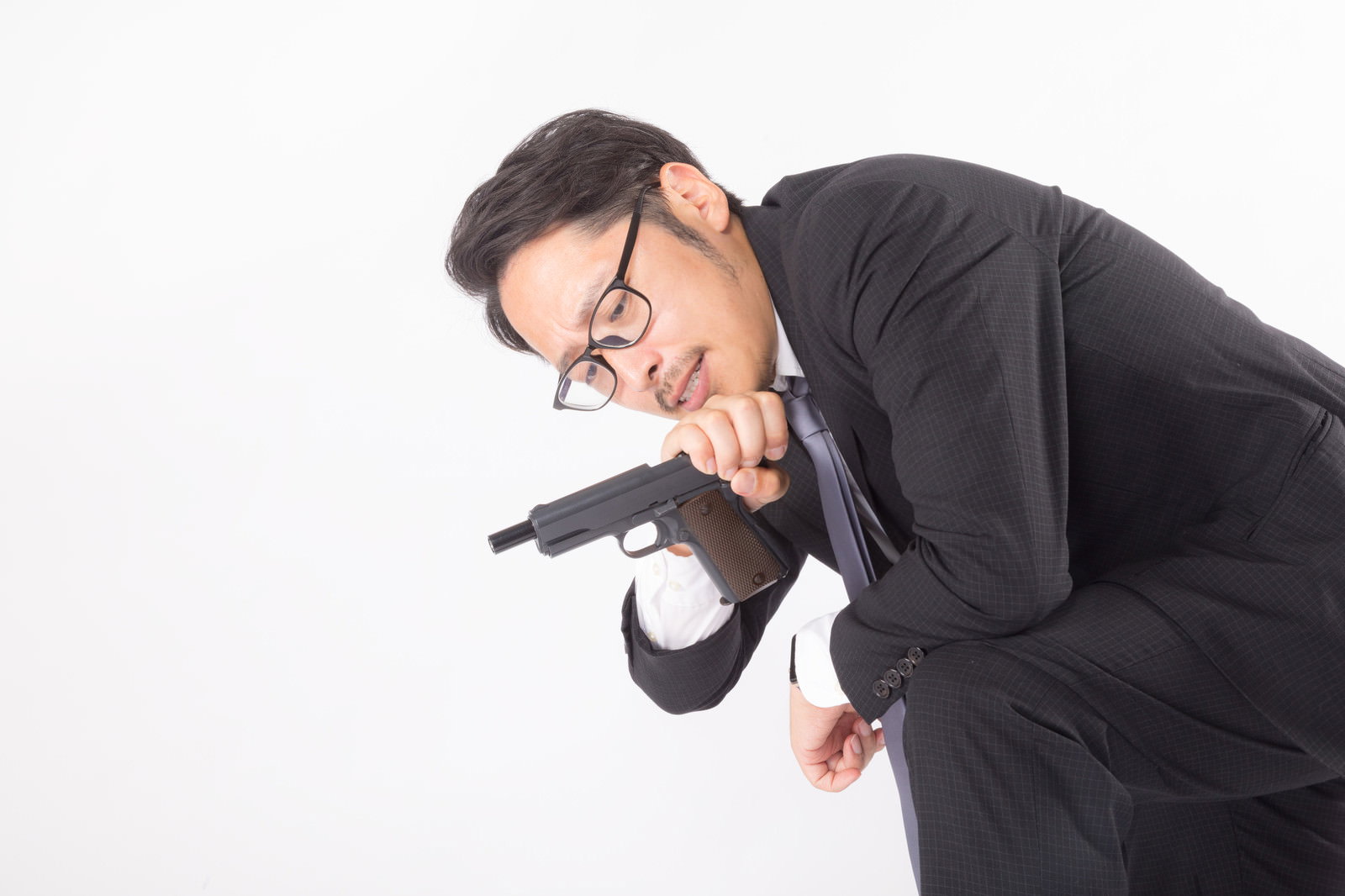 黒いスーツを着た男性が白い背景で拳銃の弾詰まりを確認している［モデル：ゆうせい］