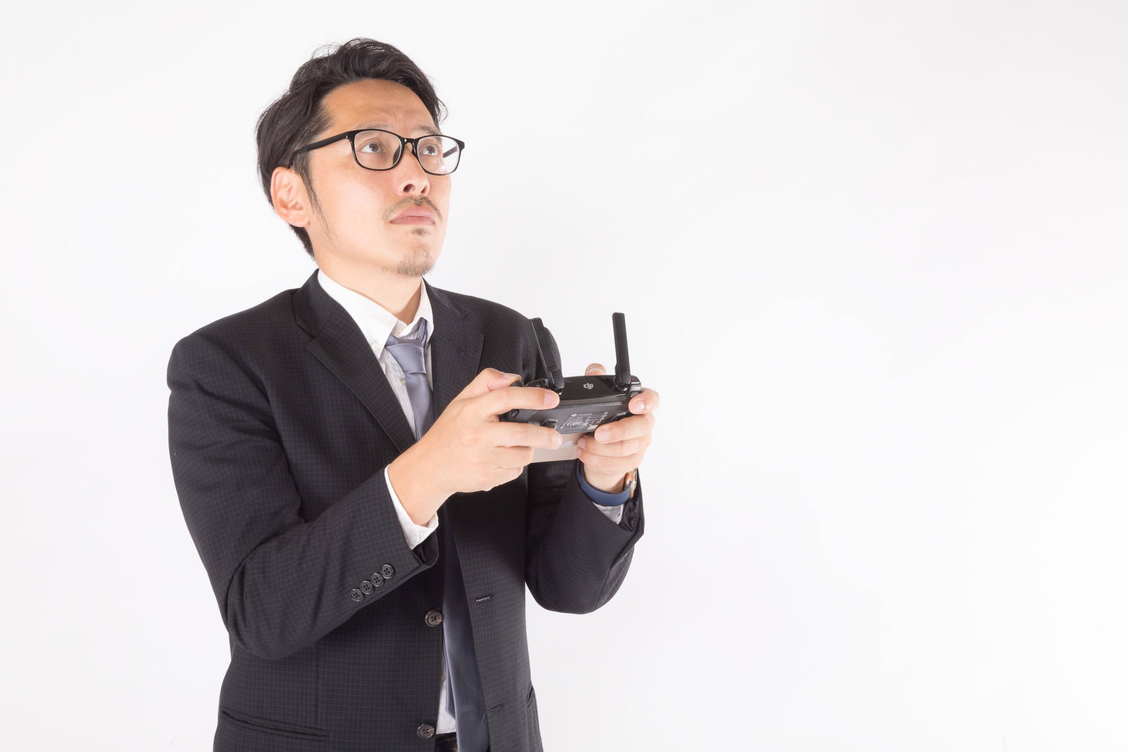 黒いスーツを着た眼鏡の男性がプロポでドローンを操縦している［モデル：ゆうせい］
