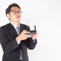 スーツ姿でプロポを手にしたドローン操縦士の写真