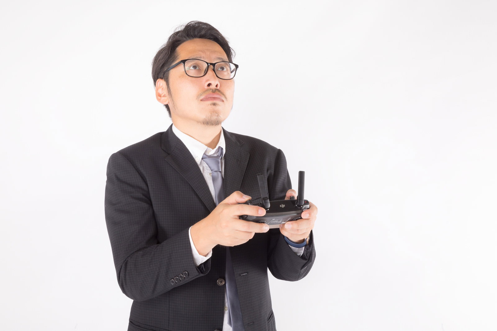 黒いスーツを着た男性がドローンのプロポを持って操縦している［モデル：ゆうせい］
