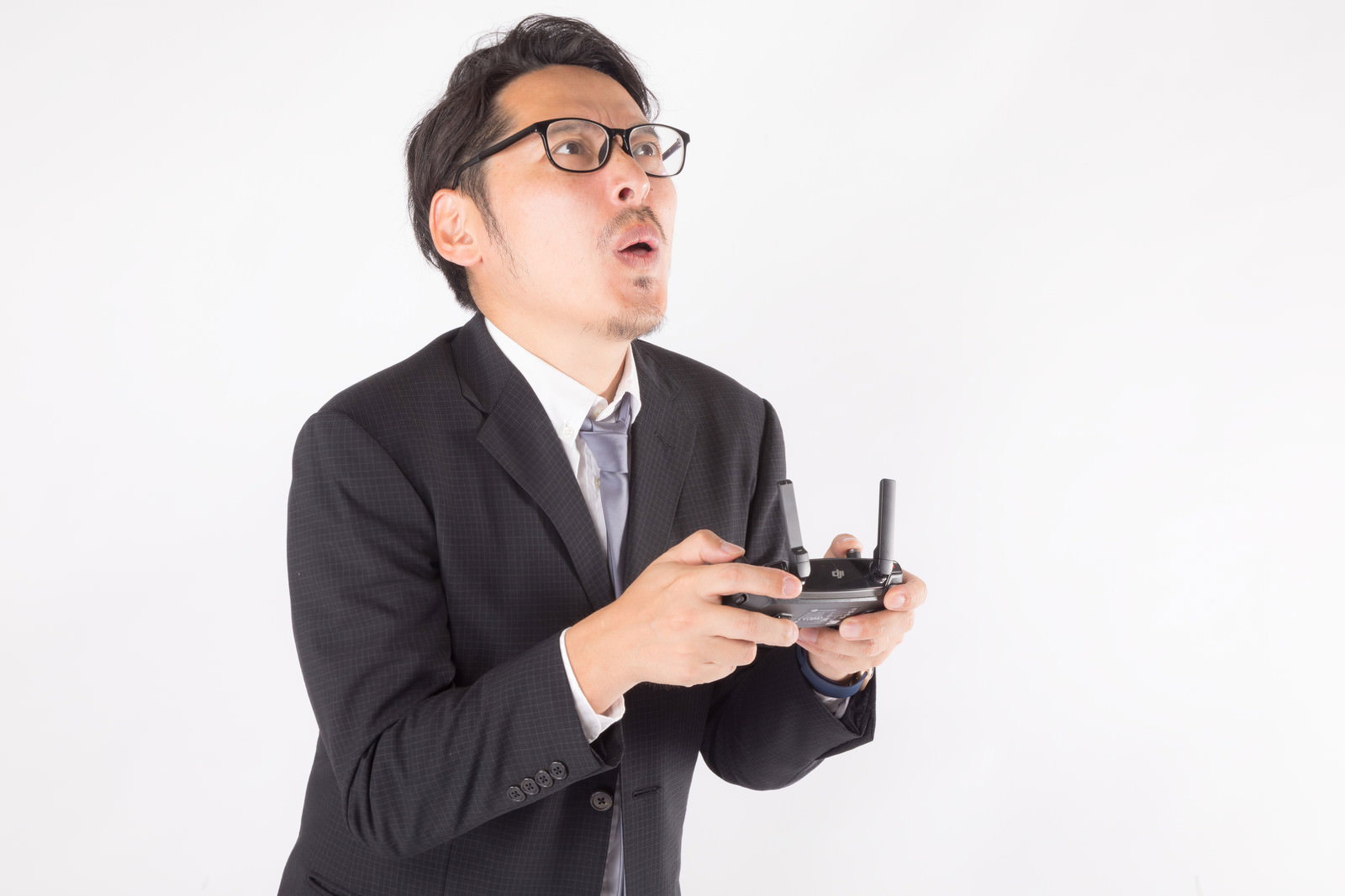 ドローンのプロポを持ちながら驚いた表情を見せるスーツ姿の会社員男性［モデル：ゆうせい］