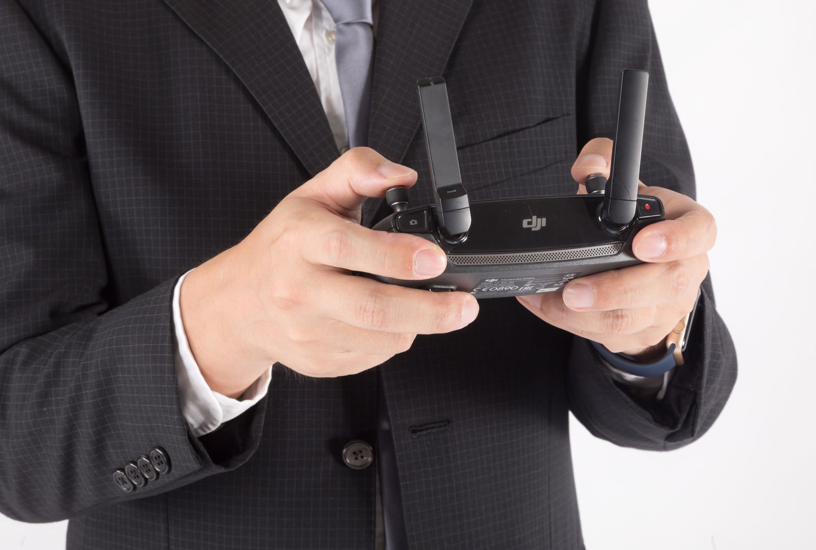 黒いスーツを着たビジネスマンがドローンのプロポを両手で操作している［モデル：ゆうせい］