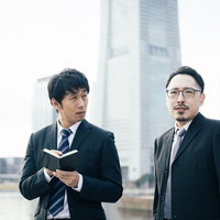 疑惑を問いただされ視線をそらすスーツ姿の男性役員の写真