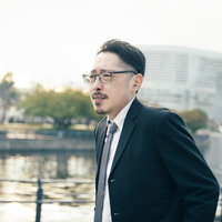 水辺で遠くを見つめるスーツ姿の上司の横顔の写真