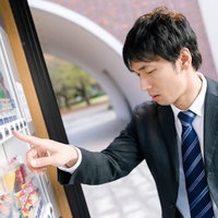 ボタンを押しても商品が落ちてこない自販機の前のスーツ男性の写真