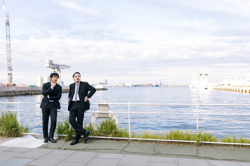 港で張り込みをするスーツ姿の刑事と記者たちの監視風景