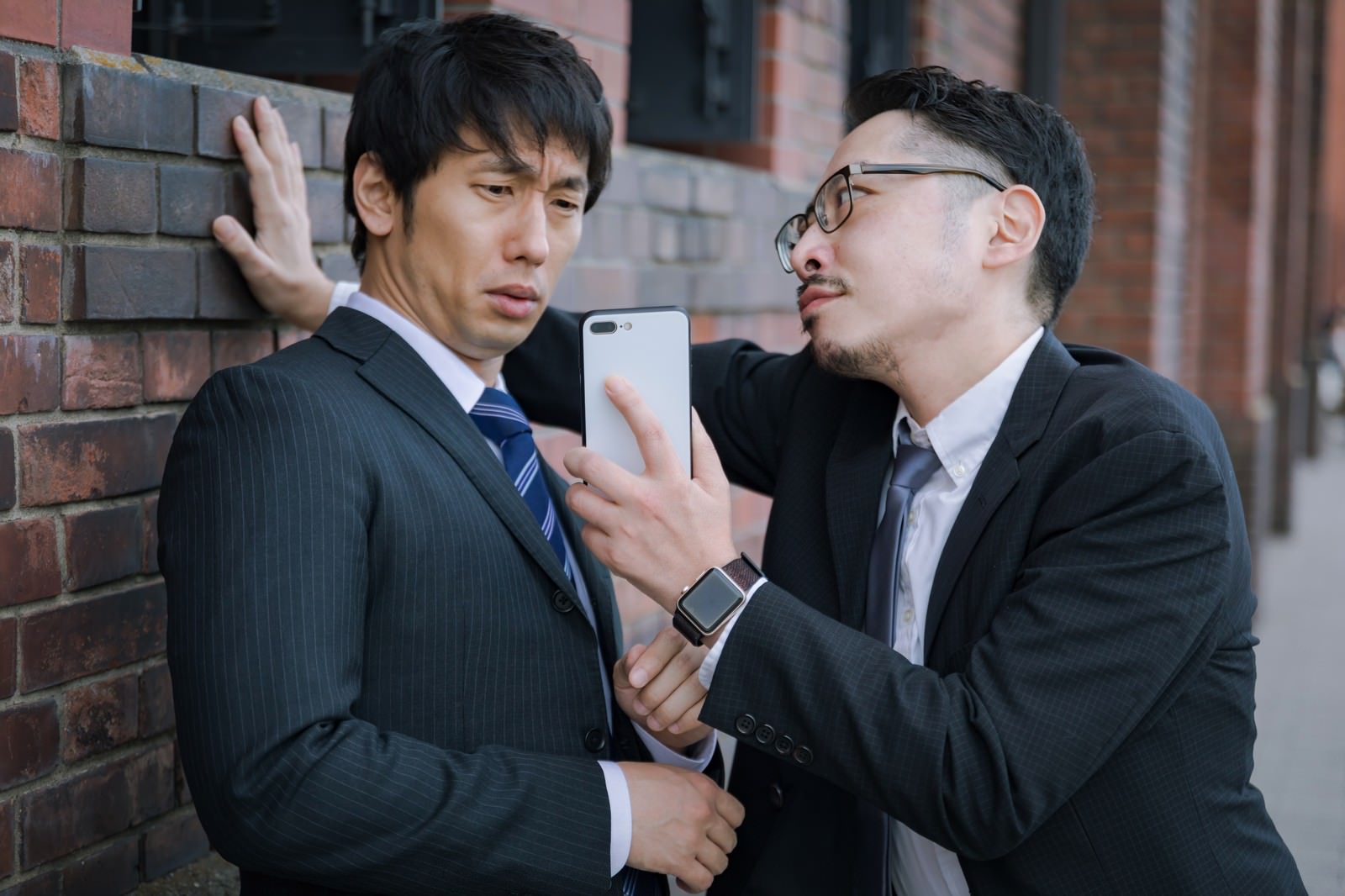 レンガの壁の前でスーツ姿の男性が壁ドンをしている場面［モデル：ゆうせい 大川竜弥］