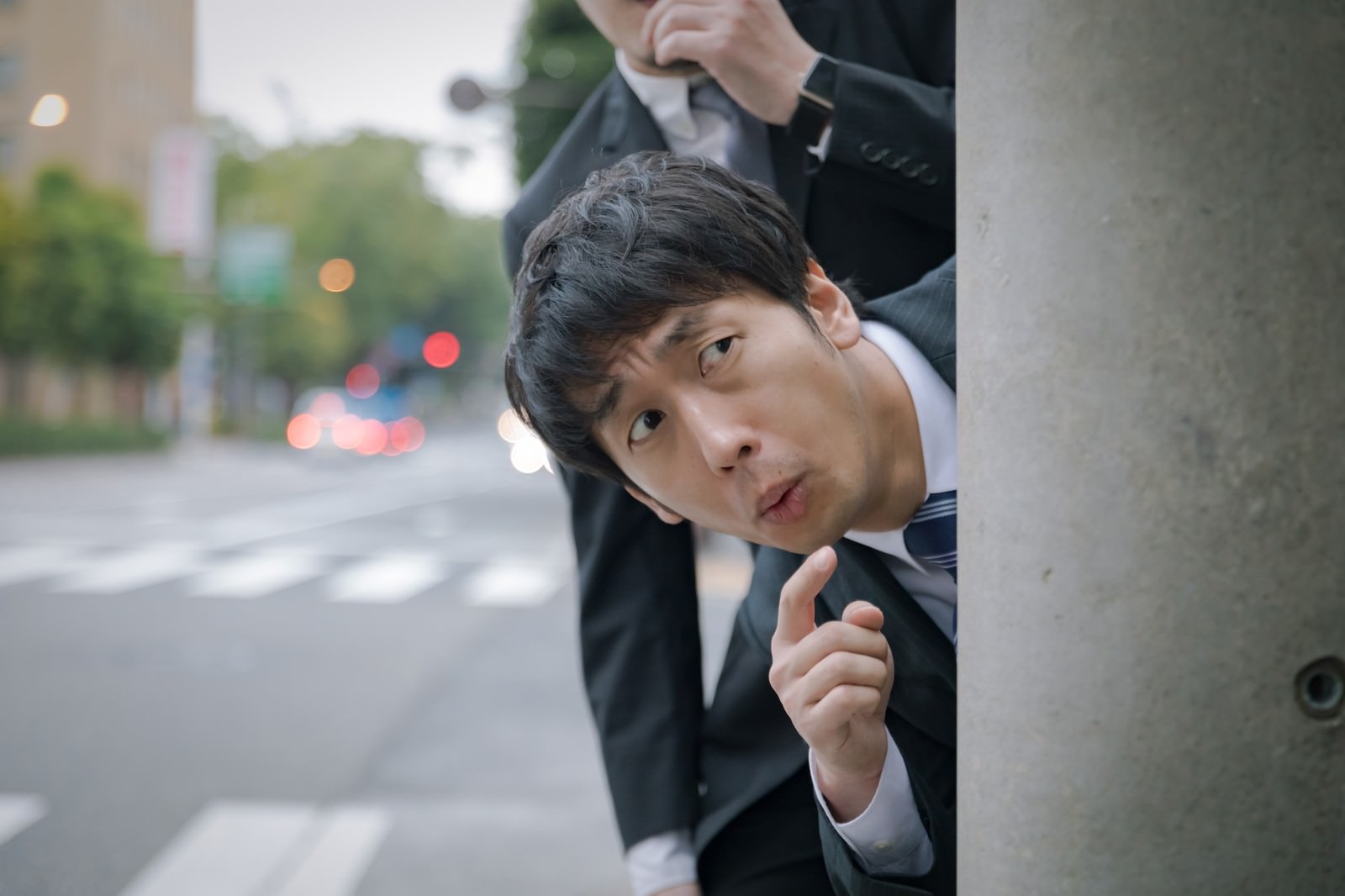 黒い服を着た男性が電柱の陰から覗いている様子［モデル：ゆうせい 大川竜弥］