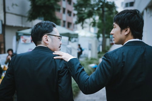 年上の部下を励ます会社員の応援シーン、肩に手を置き支援する職場のビジネス場面