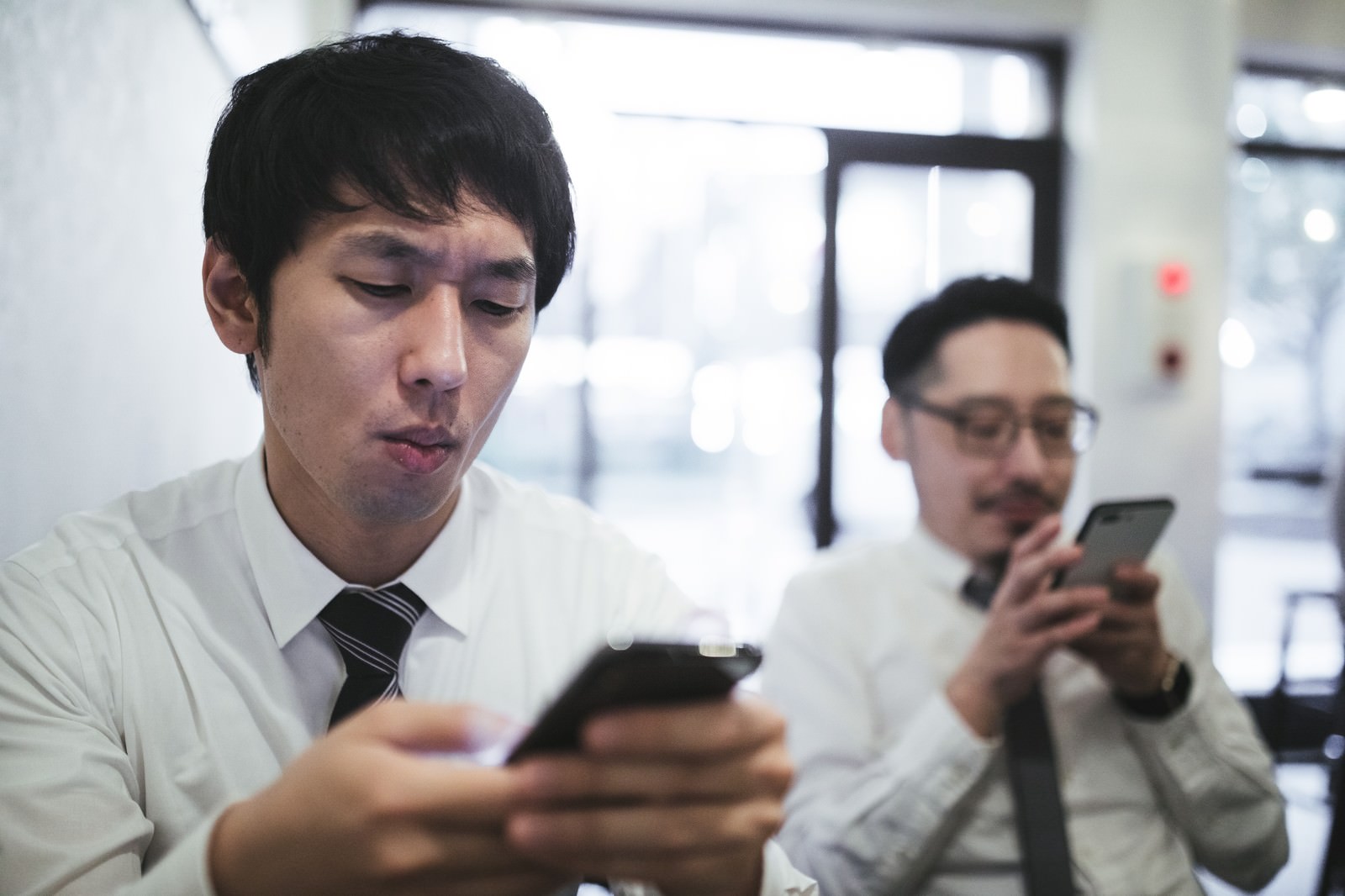 スーツを着た男性記者がスマートフォンを見ながら困った表情をしている［モデル：ゆうせい 大川竜弥］