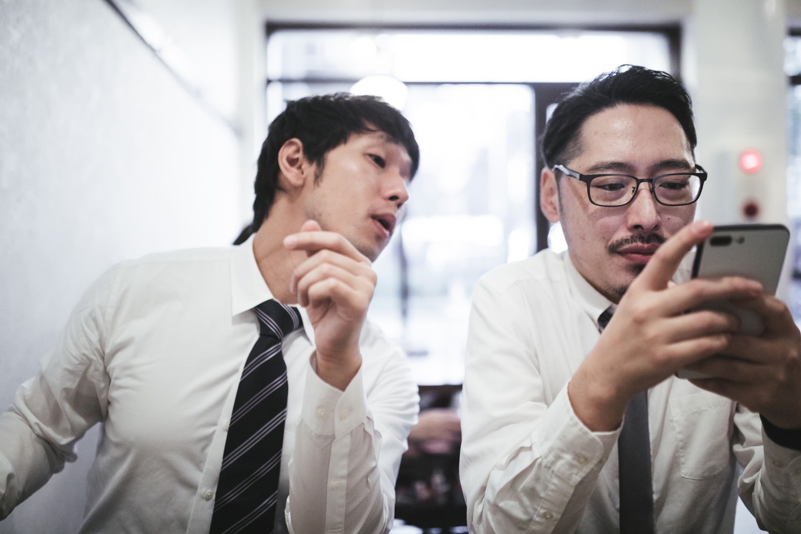 A man in a suit peering at a smartphone in an office setting