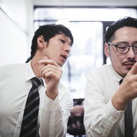 スマートフォンの画面を覗き見するスーツ姿の男性の写真