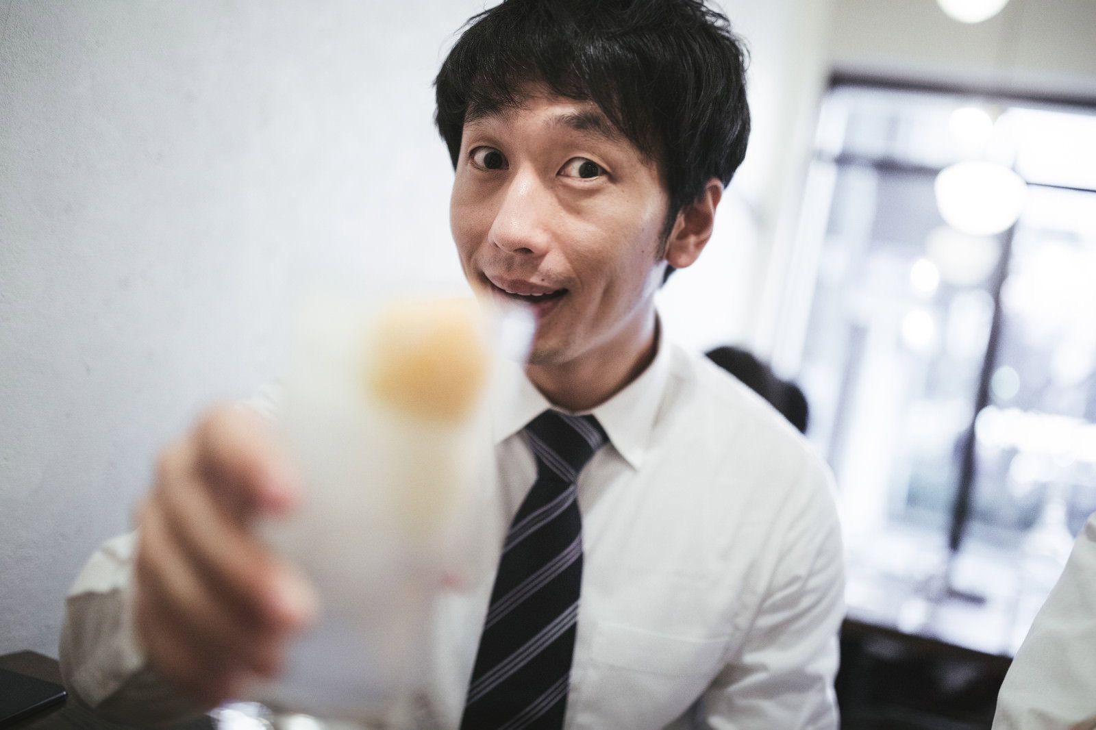 スーツ姿の男性が笑顔でグラスを持ち乾杯のポーズをとっている様子［モデル：大川竜弥］