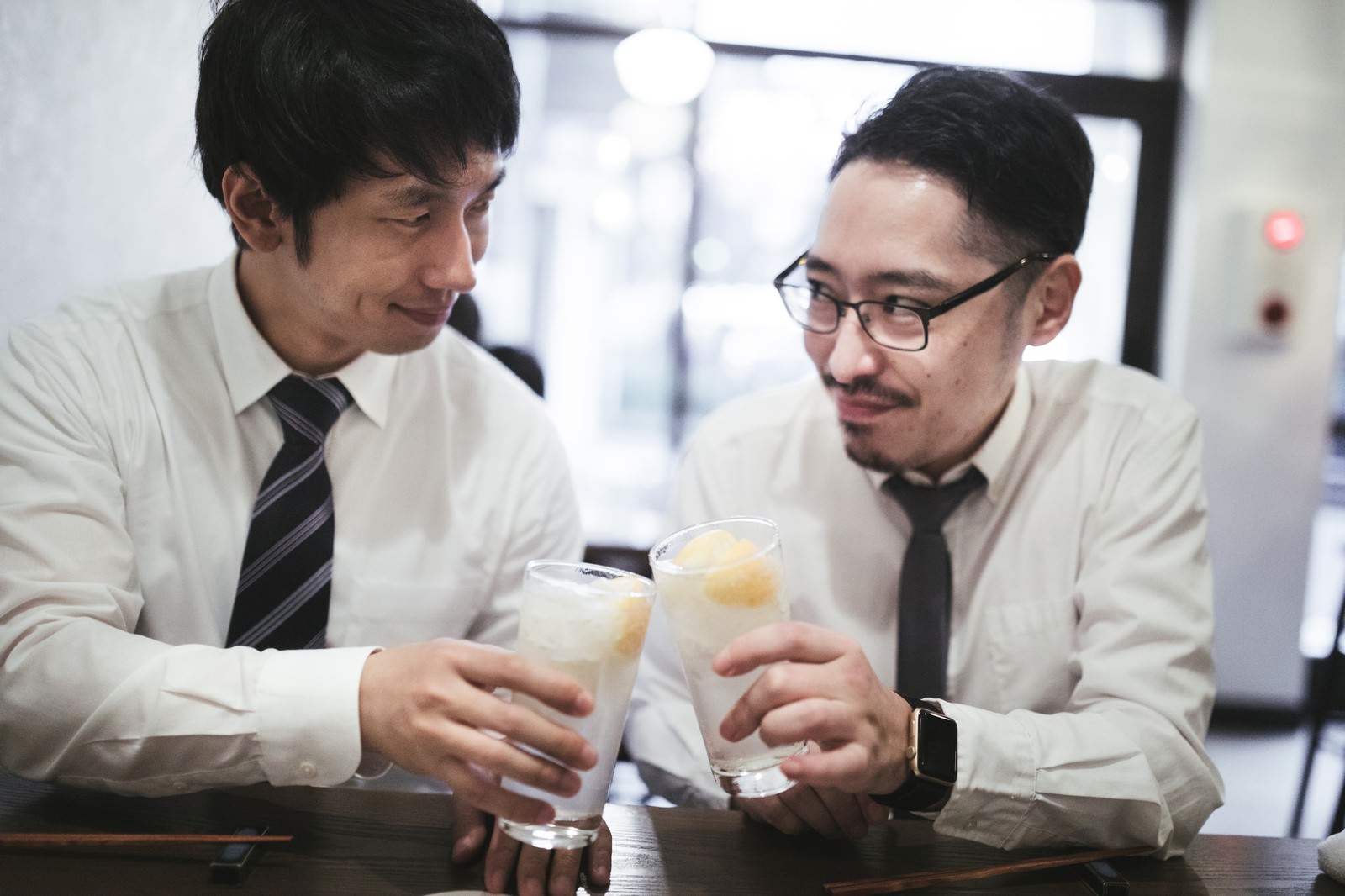 スーツとネクタイ姿の男性2人が居酒屋でレモンサワーを持ち合わせて乾杯している［モデル：ゆうせい 大川竜弥］