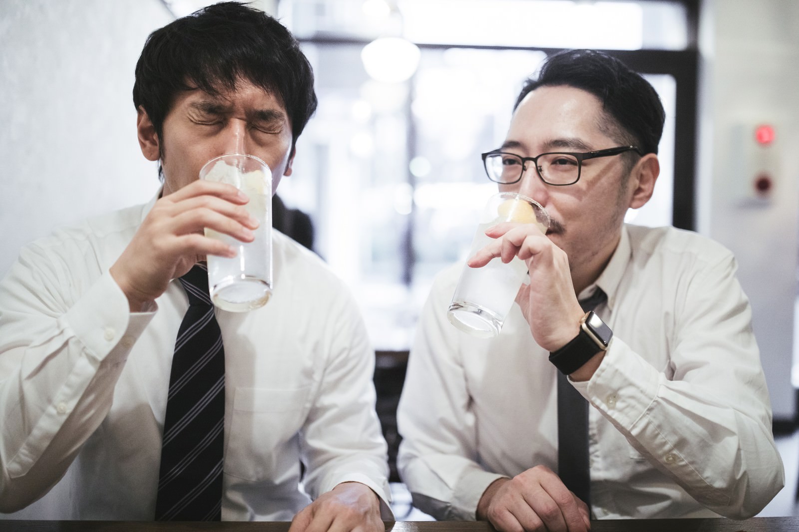 居酒屋でビールジョッキを持って乾杯するスーツ姿の会社員二人［モデル：大川竜弥 ゆうせい］