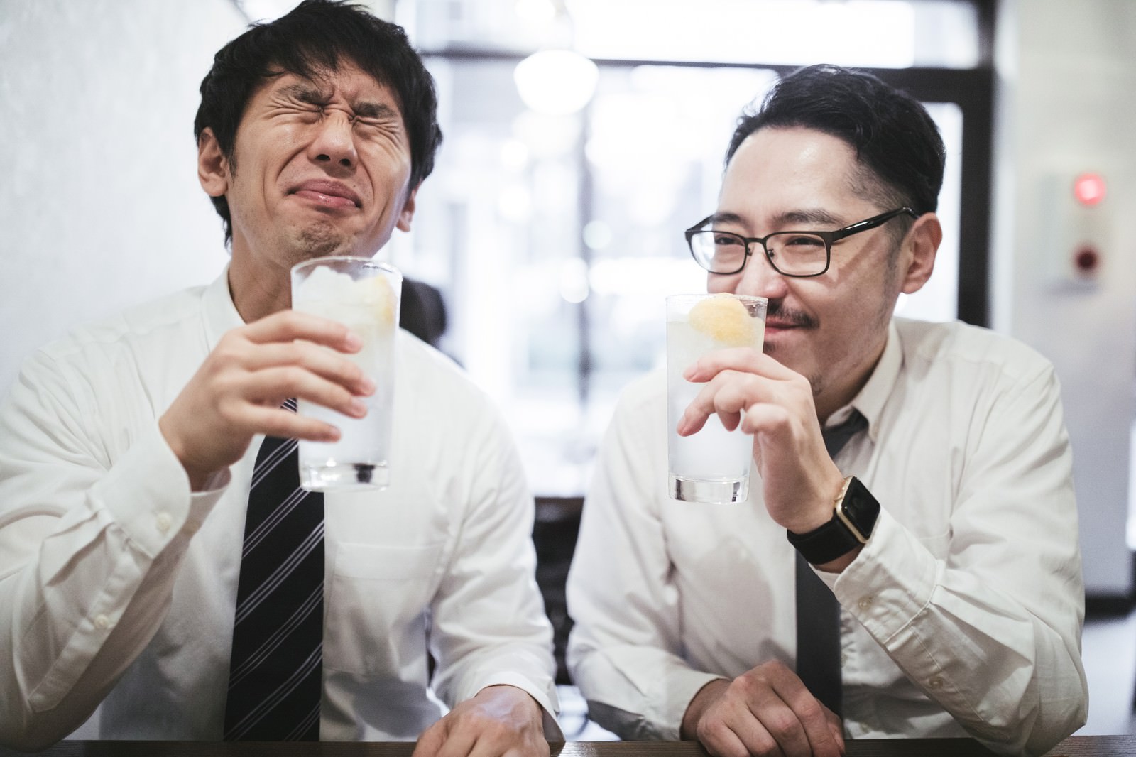 居酒屋でレモンサワーを手に乾杯するスーツ姿の男性二人［モデル：大川竜弥 ゆうせい］