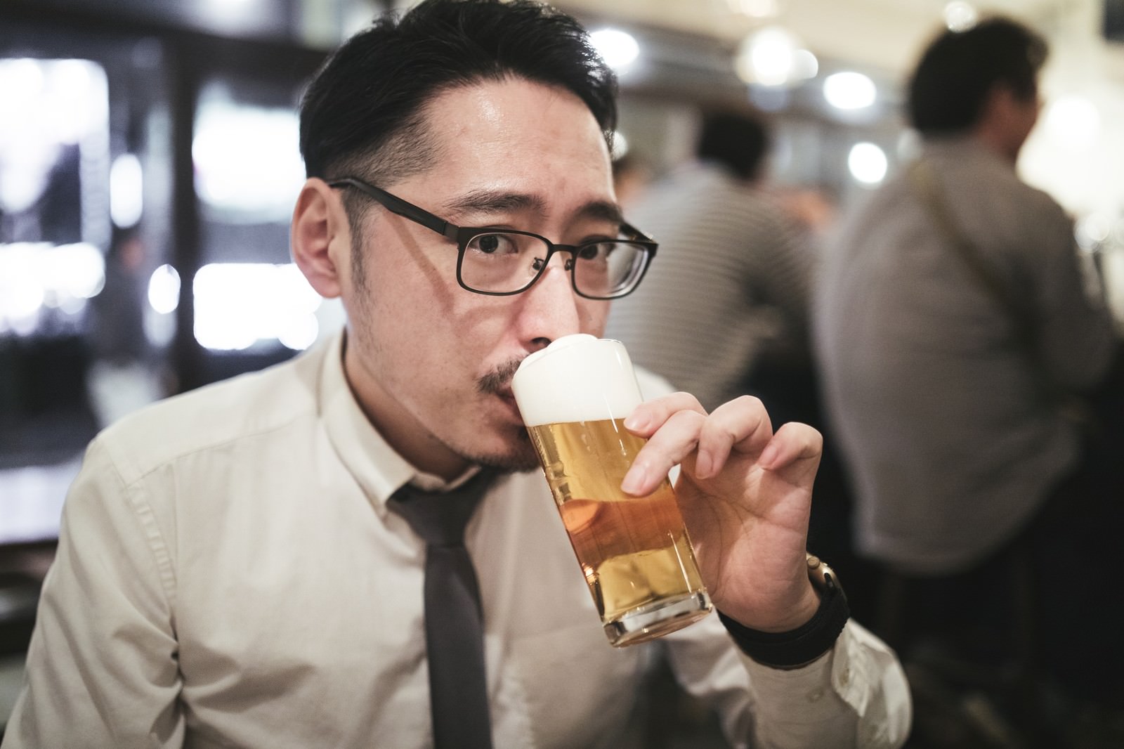 眼鏡をかけたスーツ姿の男性がビールジョッキを持って飲んでいる［モデル：ゆうせい］