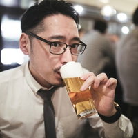乾杯前にこっそり飲むスーツ姿の男性の写真