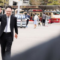 「お待たせ」と手を挙げる男性の写真