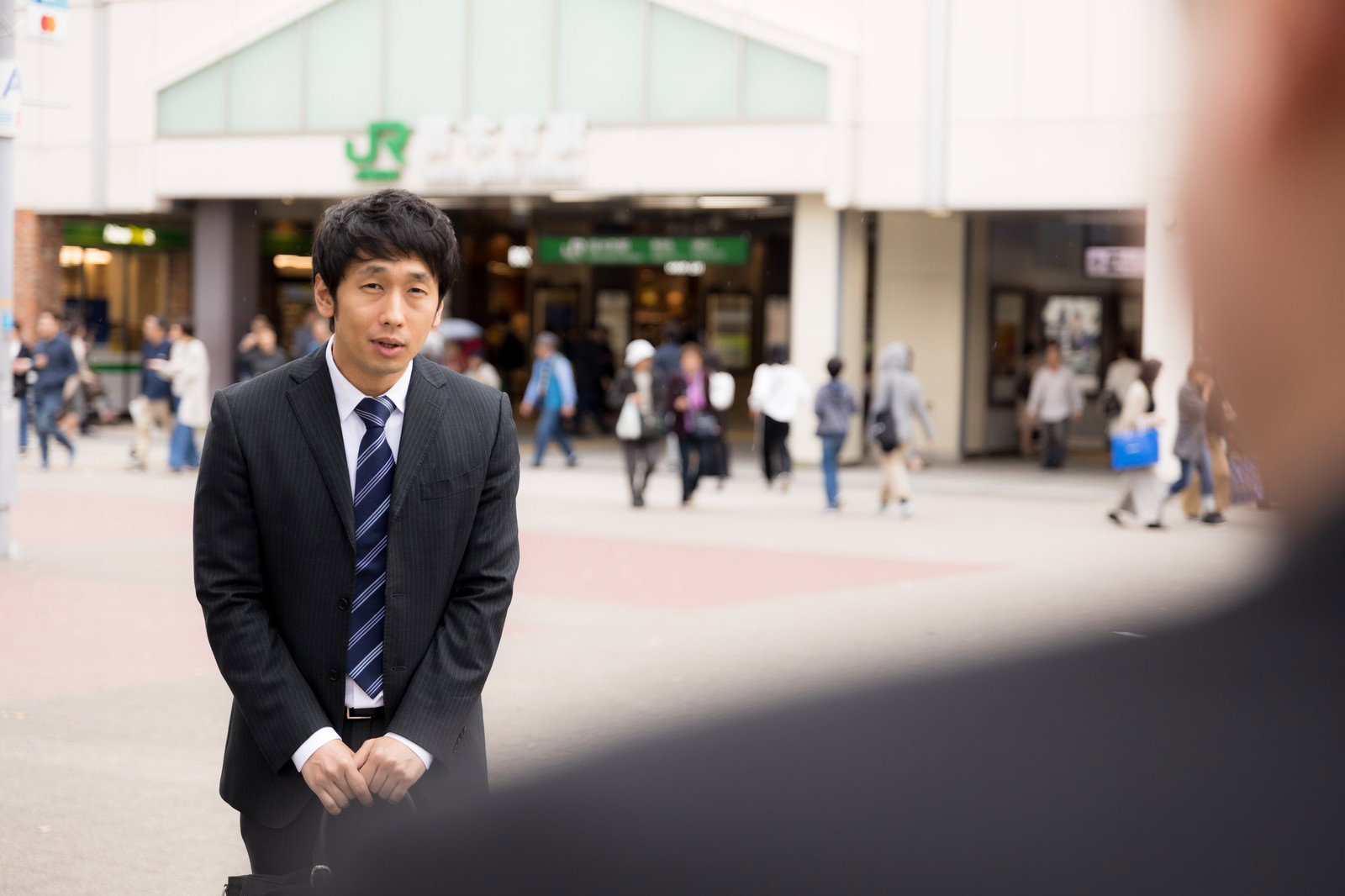 駅前で待ち合わせに遅刻して謝罪するスーツ姿の会社員男性［モデル：大川竜弥］
