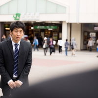 駅前で待ち合わせに遅刻して平謝りするスーツ姿の会社員の写真