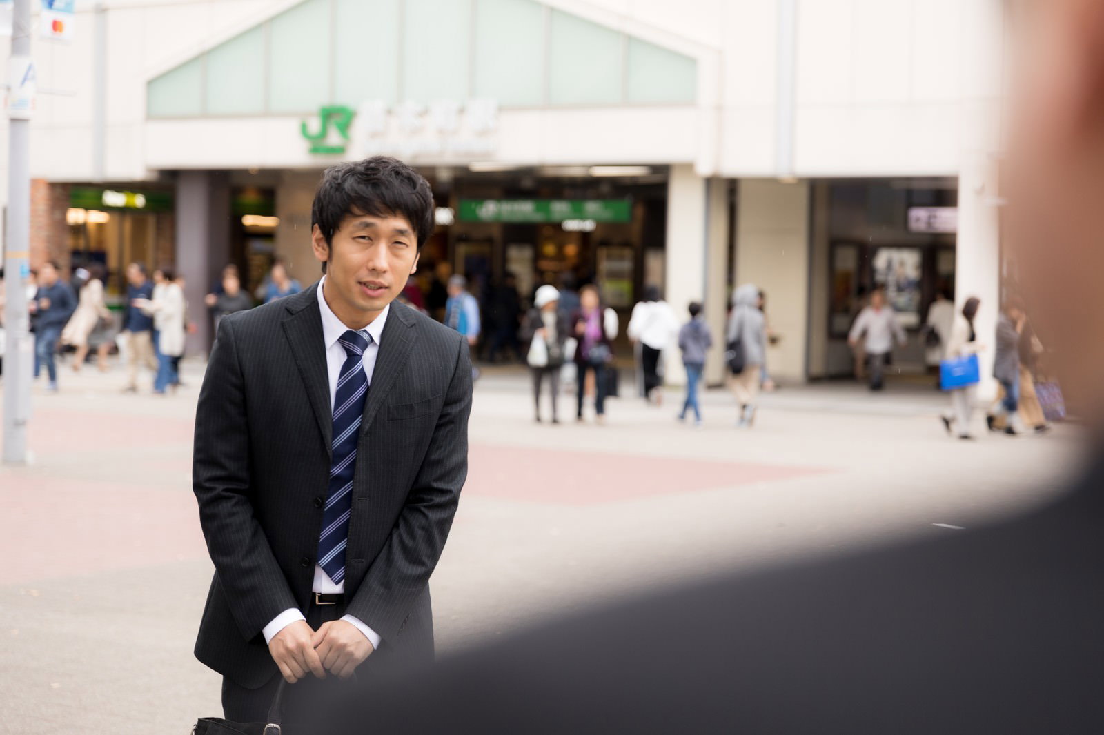 遅刻して申し訳なさそうに近づいてくるスーツ姿の男性［モデル：大川竜弥］