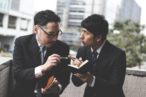 スーツ姿のジャーナリストと探偵が捜査情報を報告し合う