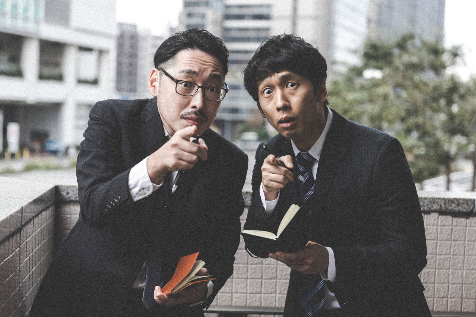 スーツ姿の男性二人が座りながら捜査について話し合っている様子［モデル：ゆうせい 大川竜弥］
