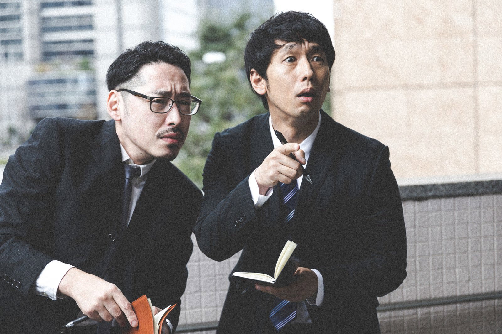 張り込み中にメモを取りながら何かを発見したスーツ姿の男性記者2人［モデル：ゆうせい 大川竜弥］