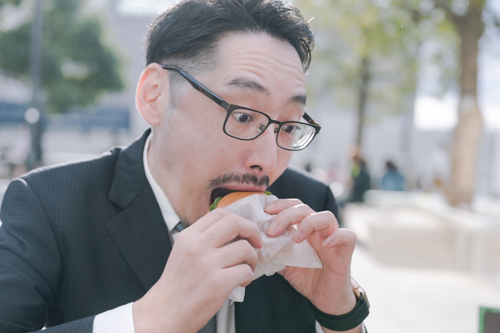 スーツ姿の男性社員がハンバーガーを両手で持ち食べている［モデル：ゆうせい］