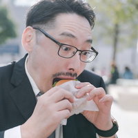 スーツ姿でハンバーガーにかぶりつく男性社員の写真