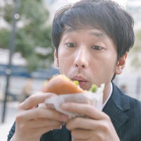 ピクルス抜いてって言ったのに、ハンバーガーをかぶりつく男性の写真