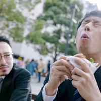 カメラが回っている時だけオーバーリアクション気味にグルメレビューするスーツ姿の男性の写真