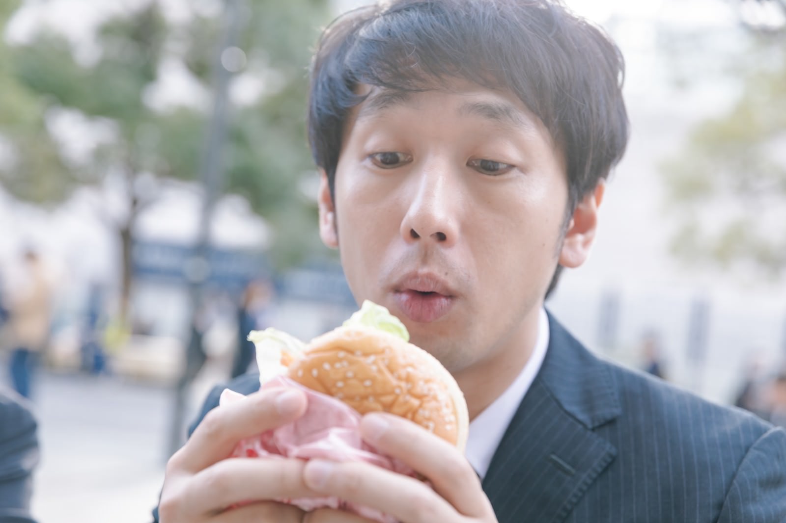 スーツ姿の会社員男性がハンバーガーを食べている写真［モデル：大川竜弥］