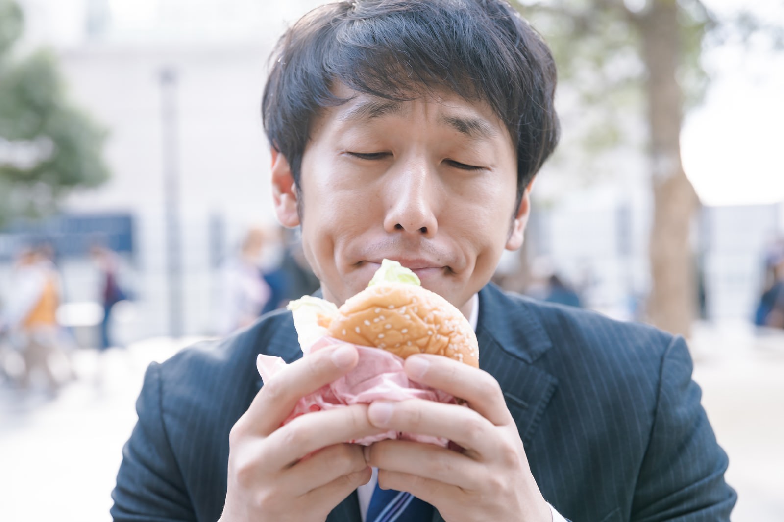 黒いスーツを着た男性が両手でハンバーガーを持ち食べている［モデル：大川竜弥］