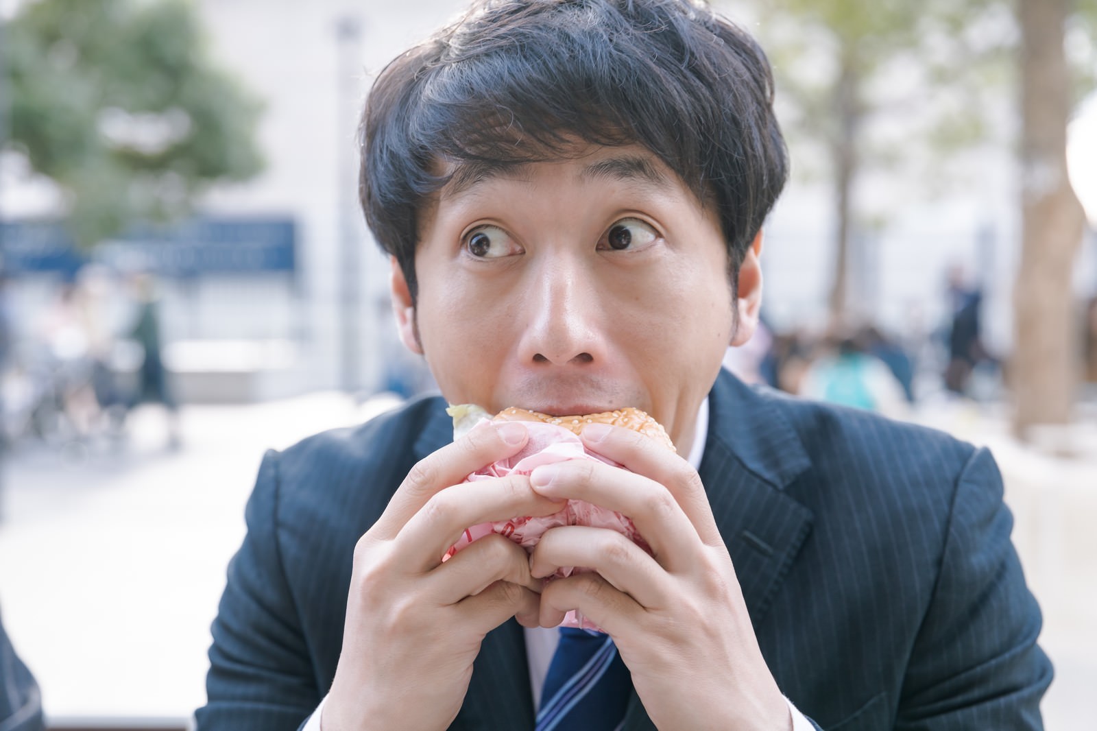 スーツ姿の会社員が両手でハンバーガーを持ち一心不乱に食べている［モデル：大川竜弥］