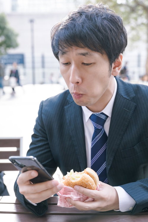 忙しなくランチにハンバーガーを食べる男性会社員
