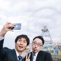 会社の先輩と観覧車をバックにセルフィーを撮る男性の写真