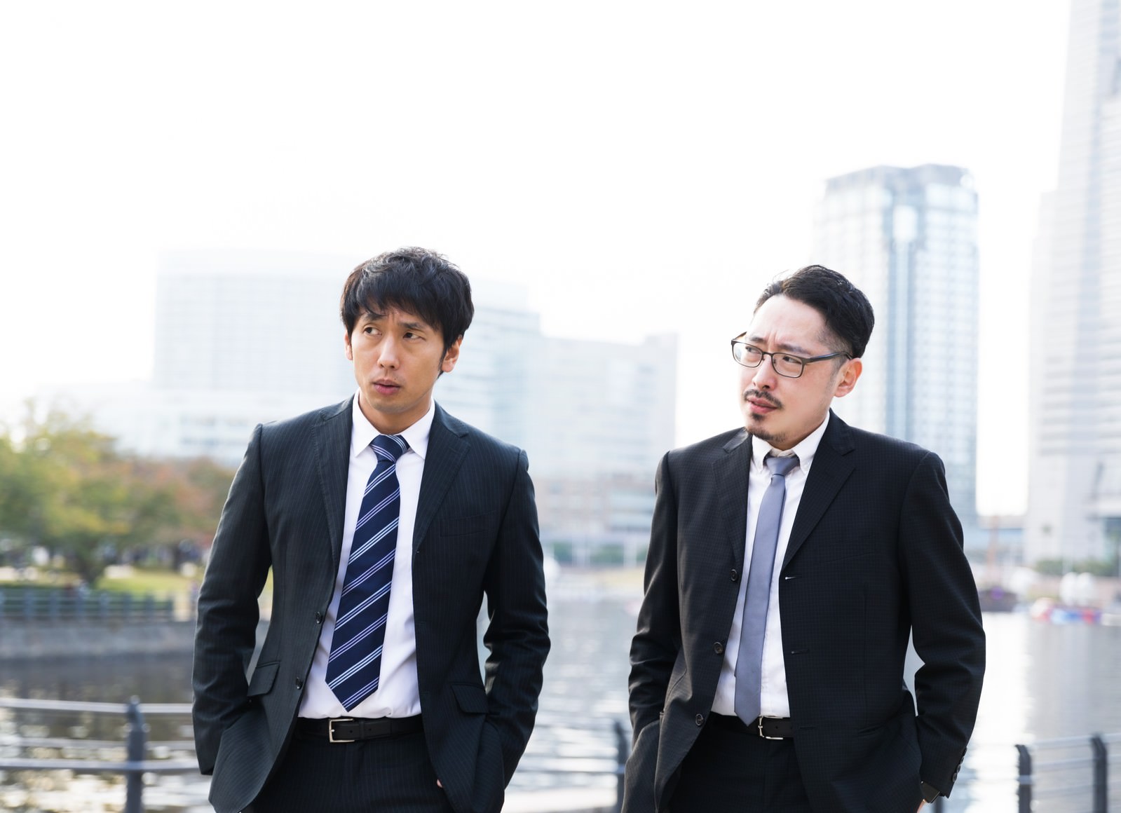 都市部の屋外でスーツを着て会話する二人の男性［モデル：大川竜弥 ゆうせい］