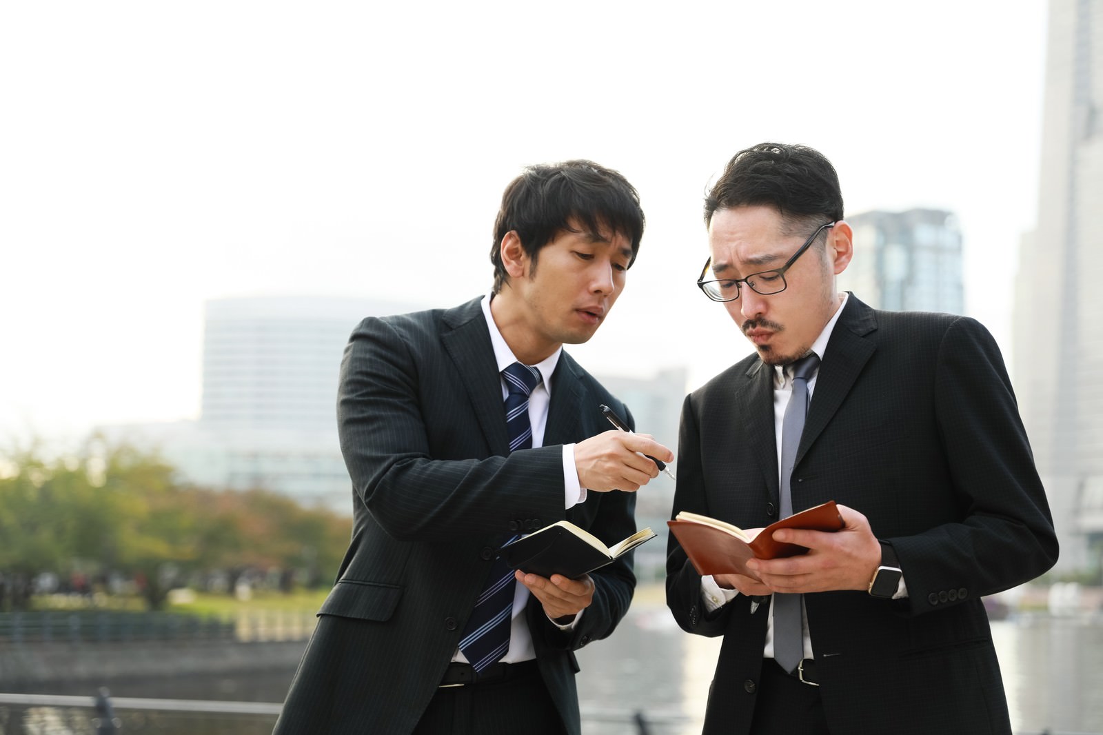 スーツ姿の男性2人が書類を見ながら打ち合わせをしている様子［モデル：大川竜弥 ゆうせい］
