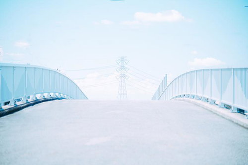 広がる青空と無機質な鉄塔、送電線が交差する都市風景