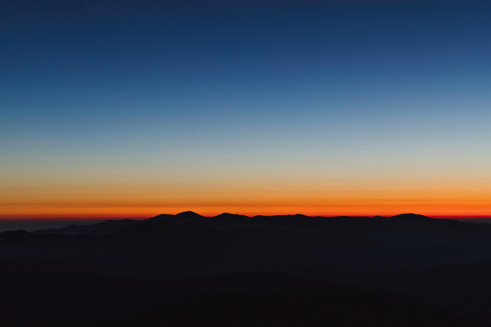 朝焼けと黄昏が重なる時間帯、山のシルエットが浮かぶグラデーション空の風景