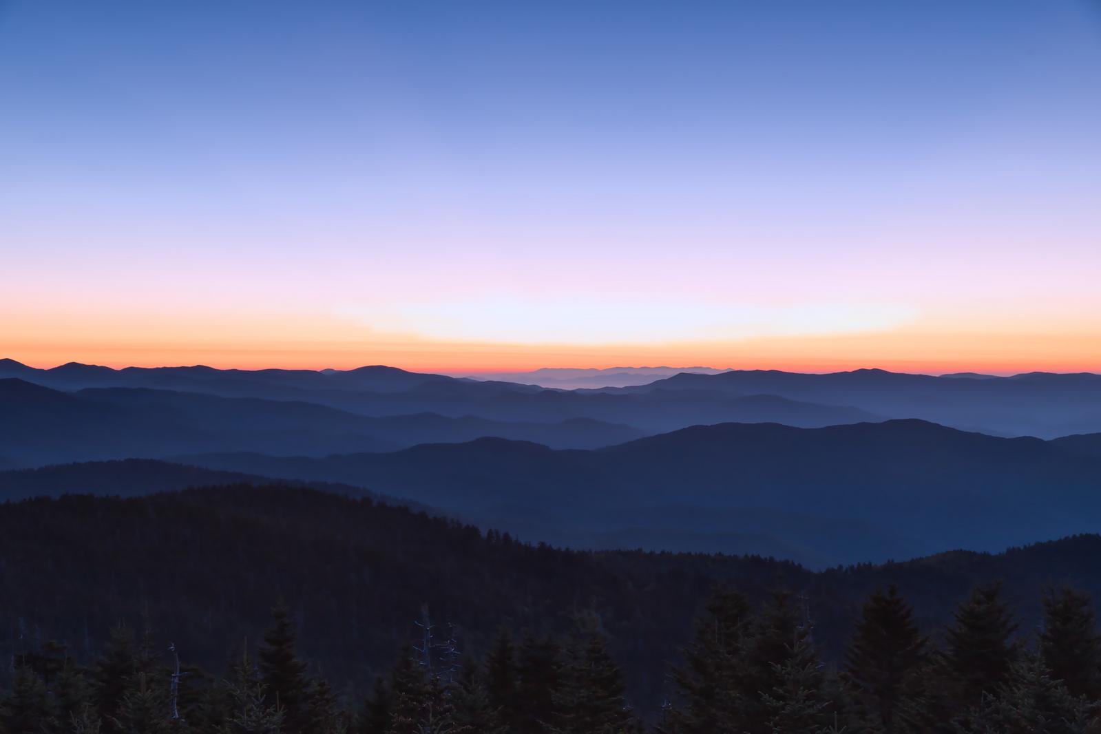 朝日で照らされ、層状に重なる山々の稜線と雲海