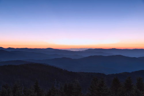 朝日で浮かび上がる重なる稜線と雲海、層状の雲が漂う山岳風景