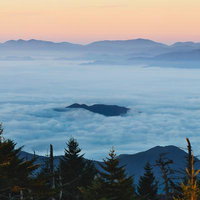 雲海から頭を出す山並みの景観、朝焼けに染まる高地風景の写真