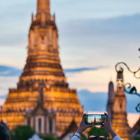 スマートフォンでワット・アルンを撮影する観光客の夕暮れ時の写真