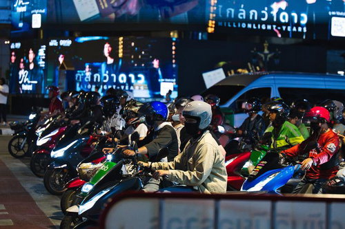 夜の街で信号待ちする多数のスクーターとバイカー