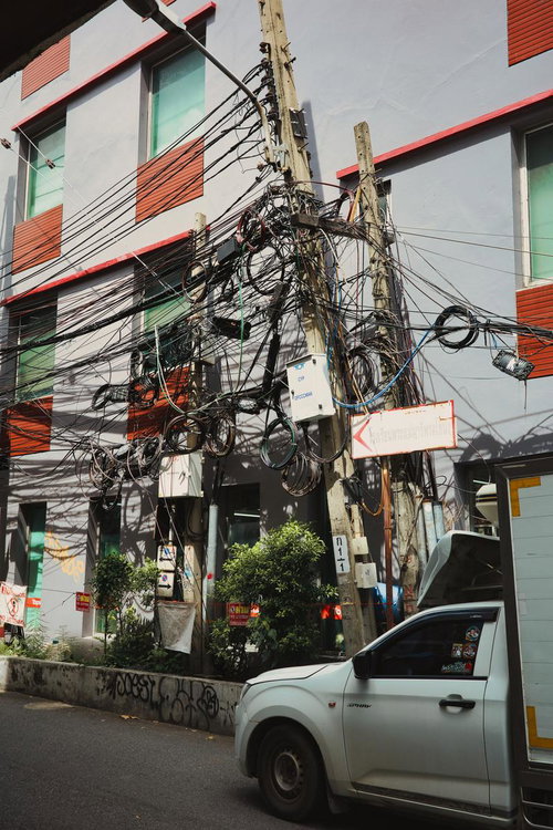 都市部の路地に立つ木製電柱に絡み合う複数の通信線と電力線