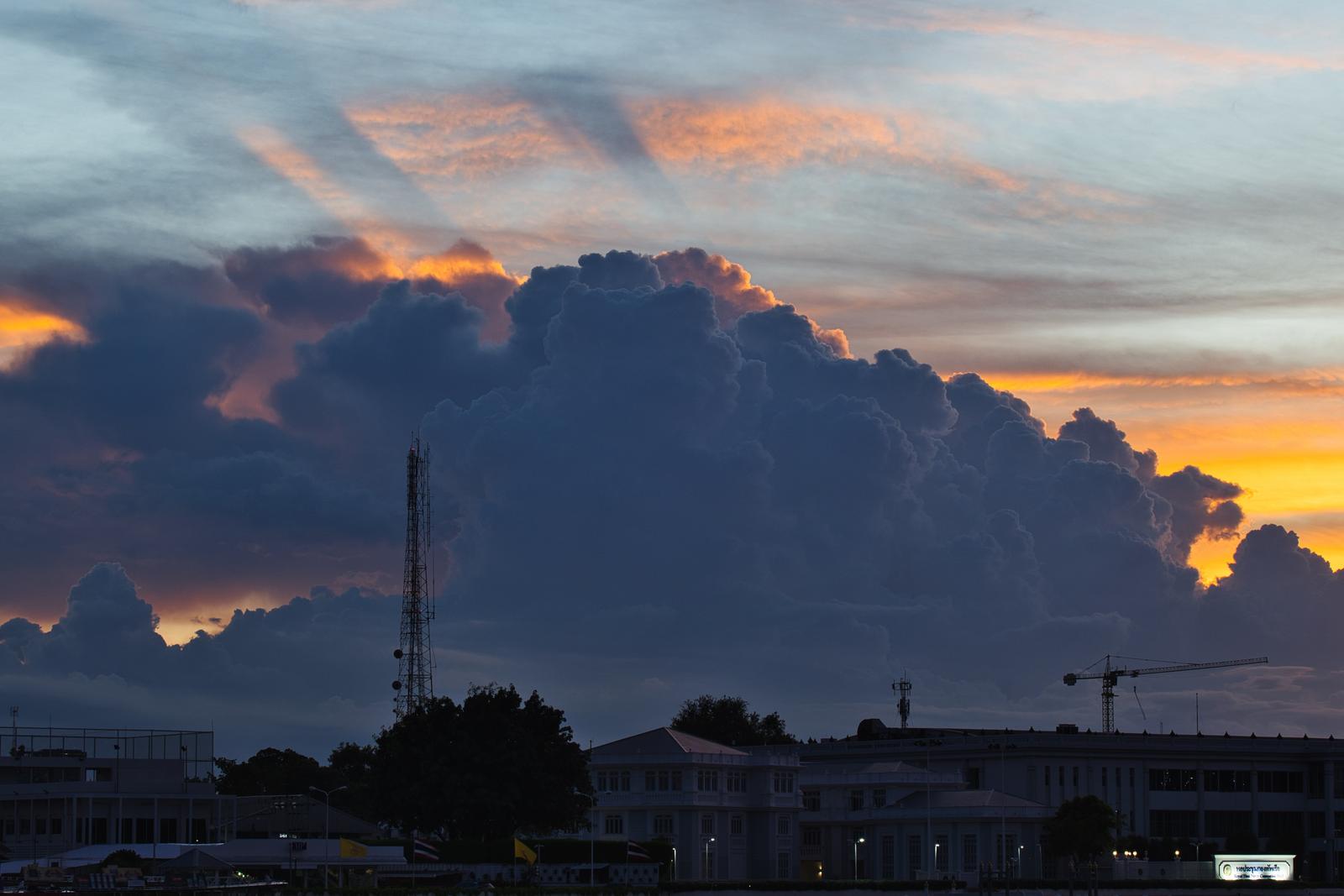 夕焼け空に立ち上がる巨大な積乱雲と都市の通信アンテナのシルエット