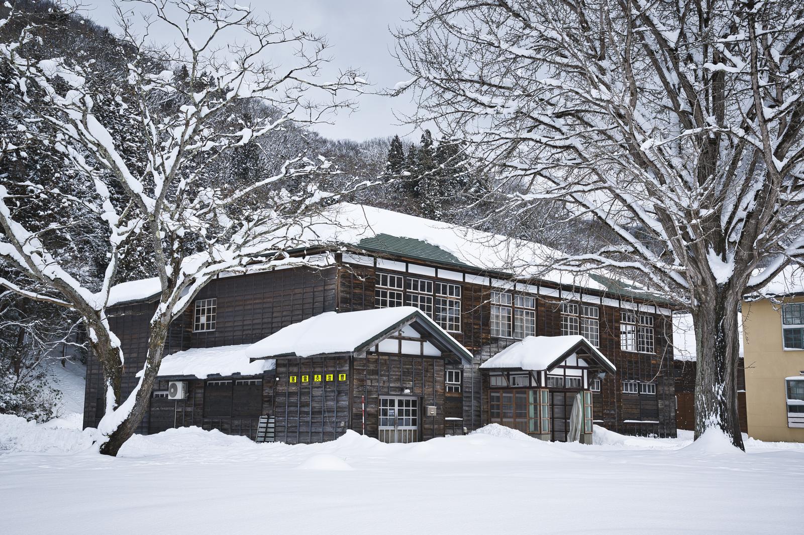 The Kugamaru Elementary School's sloped-roof buildings and multiple structures are seen through the snow-covered birch trees.